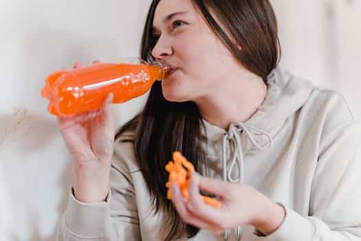 Woman with snack drinking lemonade from plastic bottle