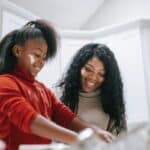 Cheerful messy African American child with flour on face cooking with parent at home