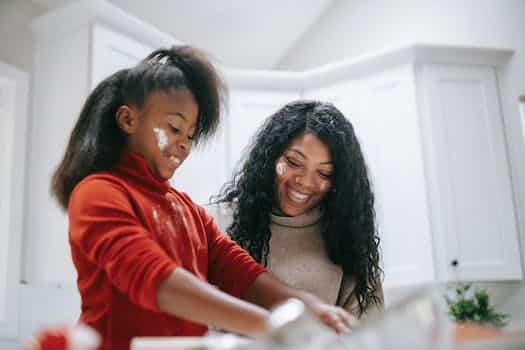 Cheerful messy African American child with flour on face cooking with parent at home