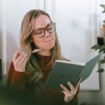 Young female bookworm having breakfast and reading novel in kitchen