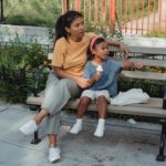 Asian mother and kid sitting on bench on street in sunny day