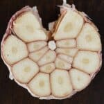 Bulb of ripe garlic in peel cut in half on wooden board