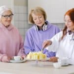 Cheerful woman cutting cake while drinking tea together with female friends