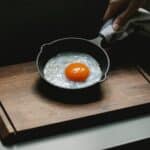 Crop anonymous chef demonstrating yummy fried chicken egg on pan placed on wooden board in dark kitchen