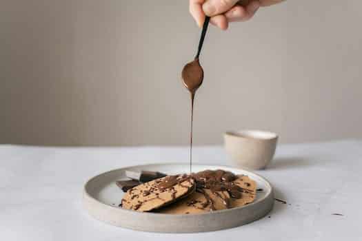 Crop unrecognizable chef pouring chocolate syrup on pancakes in plate on table on gray background