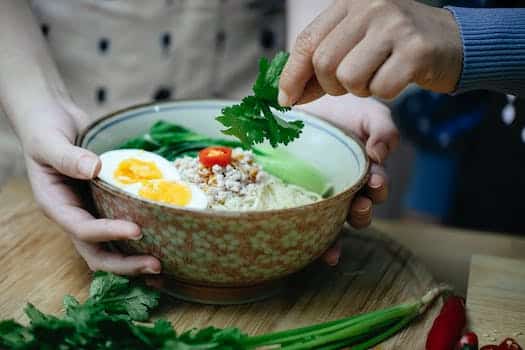 Crop unrecognizable women decorating Asian noodle soup with parsley