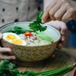 Crop unrecognizable women decorating Asian noodle soup with parsley