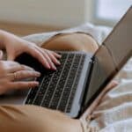 Faceless woman using laptop while sitting on bed