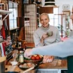 Male seasoning delicious meatballs in pan against cheerful female beloved with cup of coffee in kitchen