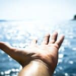 Person Hand Reaching Body of Water