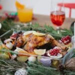 Roasted chicken on glass form with lemons and pomegranate and carrots on festive decorated table for Christmas celebration with cocktails and candles