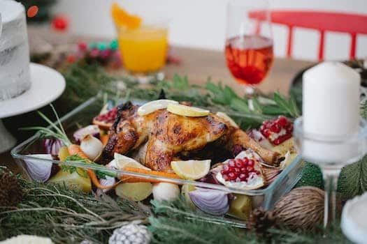 Roasted chicken on glass form with lemons and pomegranate and carrots on festive decorated table for Christmas celebration with cocktails and candles