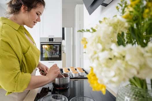 Side view of young female in apron cooking on stove berry filling for cupcakes in kitchen