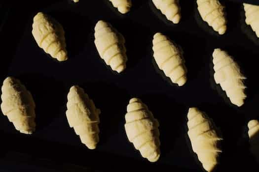 Top view composition of uncooked raw croissant dough arranged on surface of black glass in dark light