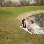 Women Lying on a Picnic Blanket Near the Lake of a Forest Park while Having a Conversation