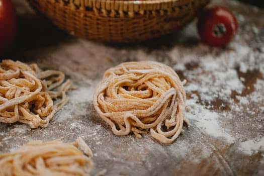 From above nests of fresh homemade uncooked spaghetti placed on wooden table with scattered flour in kitchen