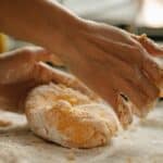 Unrecognizable woman kneading fresh dough on wooden table with flour while preparing food in kitchen