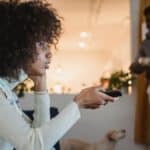 Young black woman watching TV with interest near boyfriend standing in room