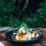 Appetizing fried eggs covered with verdant parsley in plate on timber round shaped table near trees