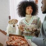 Smiling black loving couple having lunch on sofa and communicating near cute dog